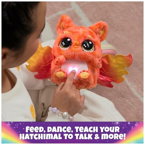Child playing with an orange plush Hatchimal toy with glowing belly.