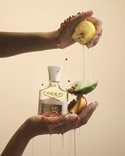 Hands squeezing lemon and apple over a Creed fragrance bottle.