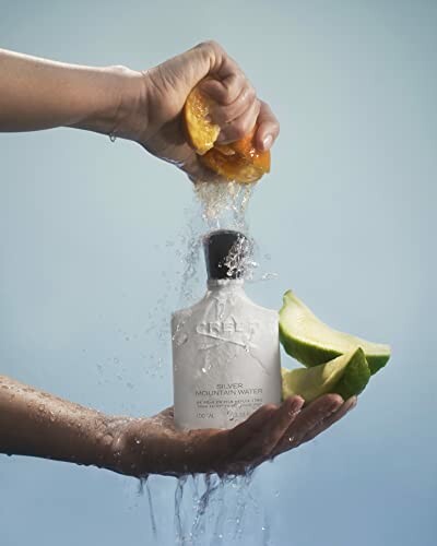 Hands squeezing an orange over a perfume bottle with lime slices.