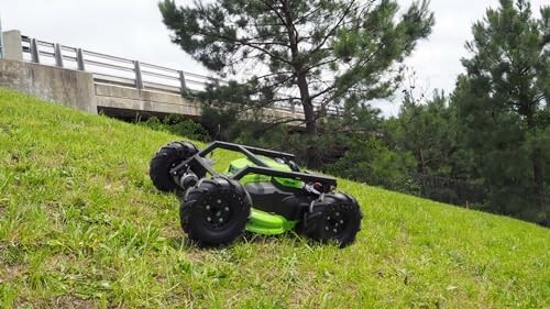 Robotic lawn mower on a grassy hill near a bridge.